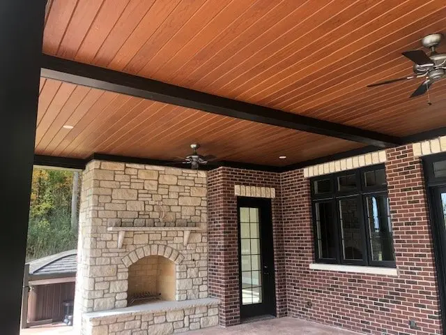Covered patio with an AFX woodgrain aluminum ceiling and stone fireplace